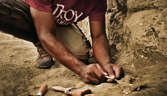 Anthropology student digging for bones in the dirt/rocks. 