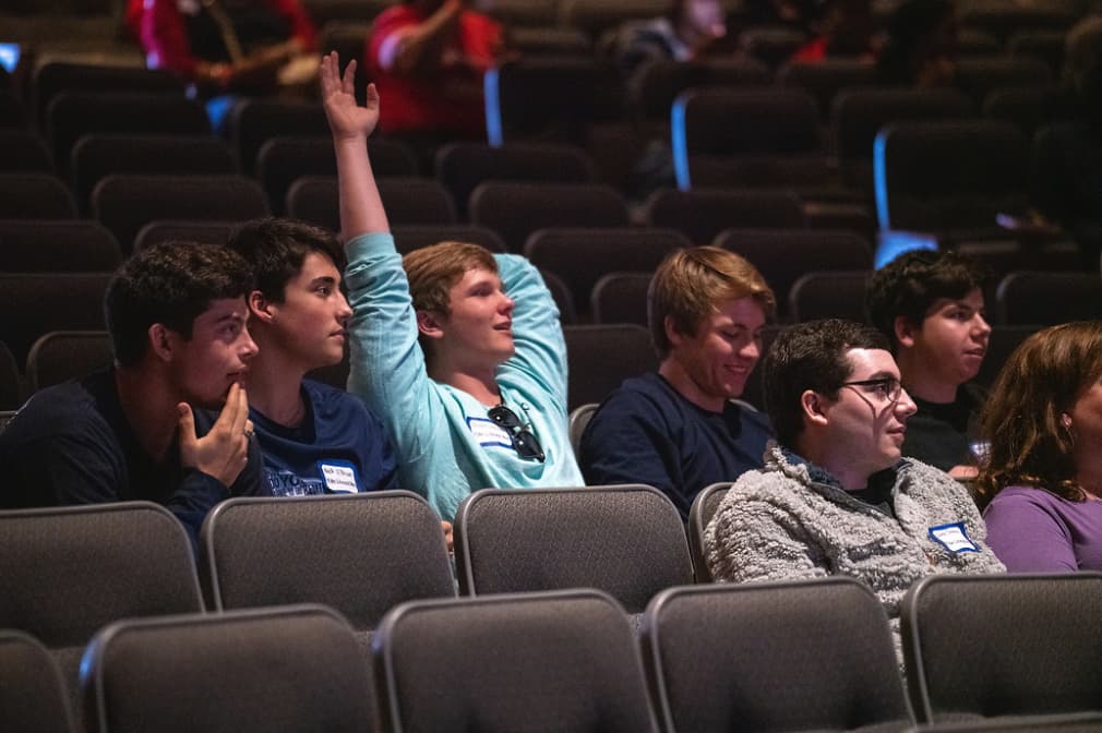 High school student raises his hand to answer questions during Geo Day closing session