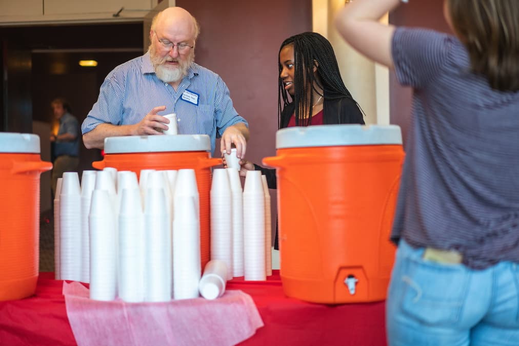 Troy Faculty member assists female high school student obtain water at breakfast prior to Geo Day opening session