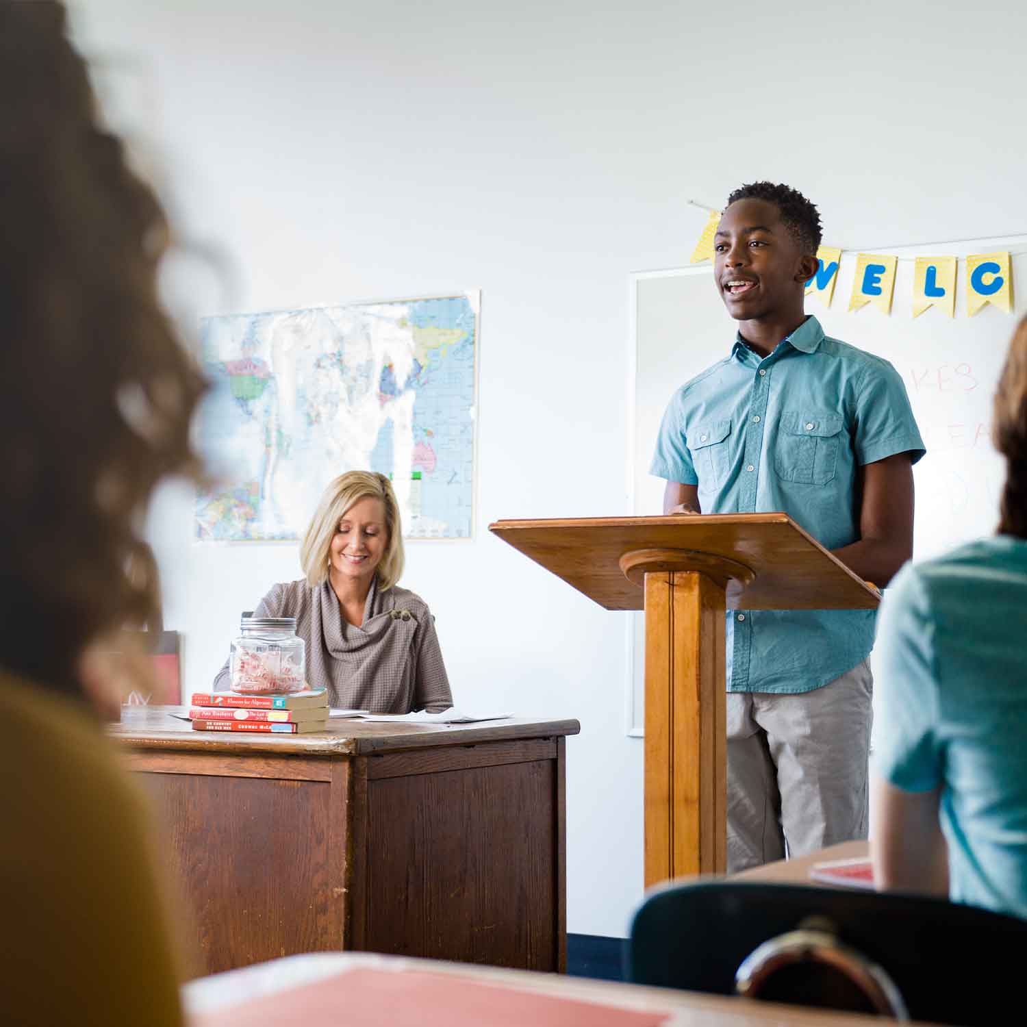 Student giving a speech from a podium with teacher assessing 