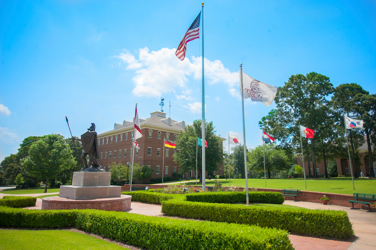 Adams building with flags flying and TROY's Hector Statue with a blue sky and green shrubs