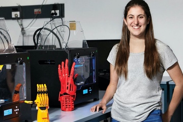 University student stading in front of 3D printed prosthetic hands and 3D printers.