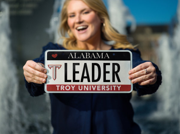 Student holding an Alabama license tag reading: Leader - Troy University