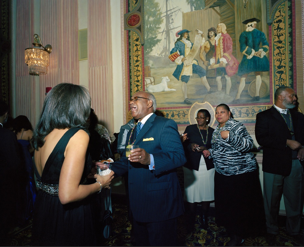 Adults in formal wear gather in conversation, the central subject laughing.