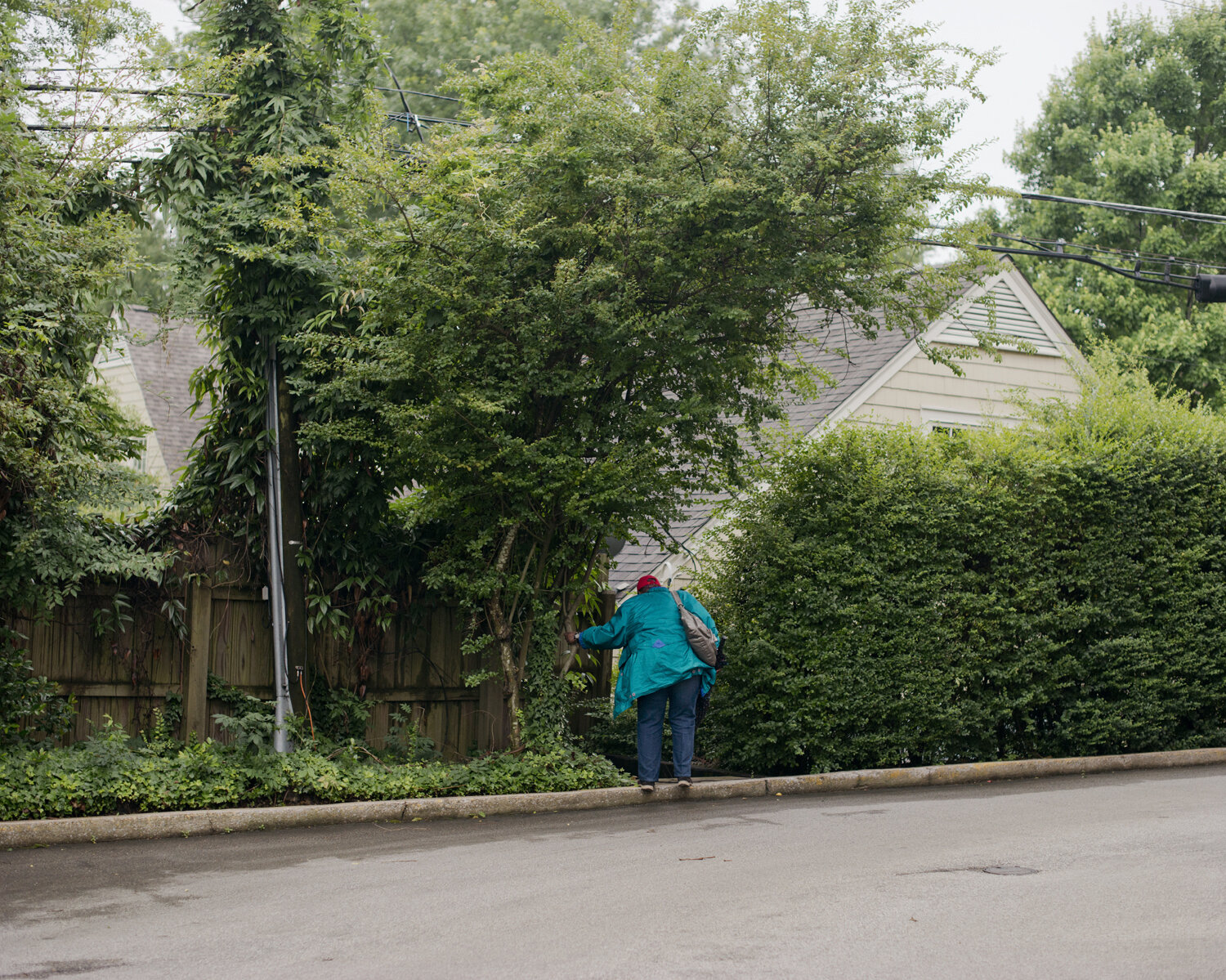 Woman stands on curb facing away from camera, her hand resting on a tree for balance.