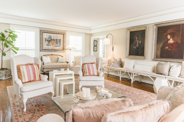 An alternate view of the formal living room offers a unique view of the two portraits hanging above the wooden bench against the wall opposite the fireplace. 