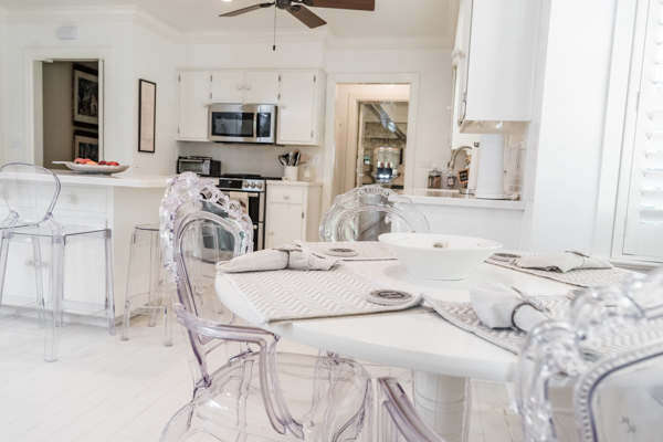 A view from the eat-in, white breakfast room table with acryllic chairs through to the kitchen inside the residence of the Chancellor of Troy University. 