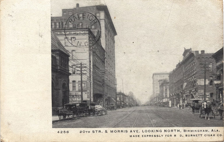 Black and white print of 20th Street in Birmingham, Alabama showing multi-story buildings and streetcar rails. Postmarked Birmingham December 14, 1905 and Raleigh, N.C. December 15, 1905.