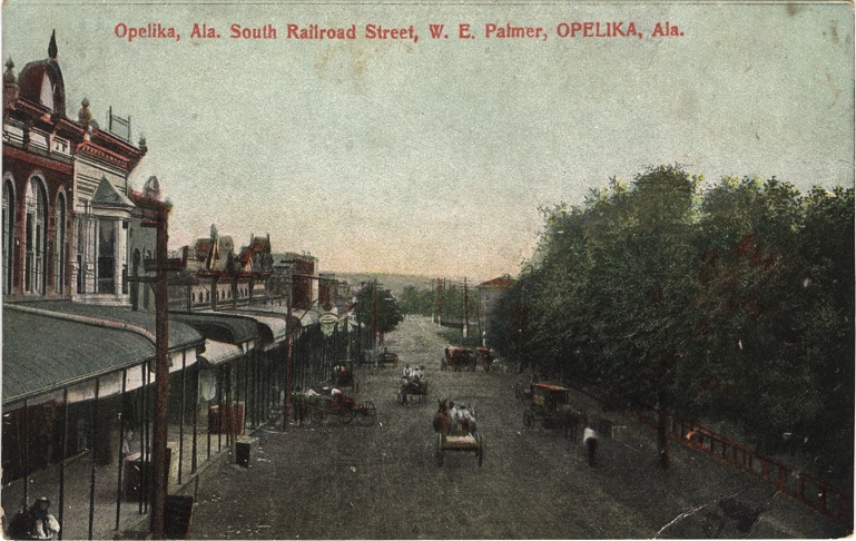 Color print of commercial buildings on unpaved Railroad Street in Opelika, Alabama.