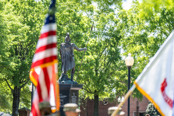 Green campus photo with the US flag in the foreground and the trojan statue in the background