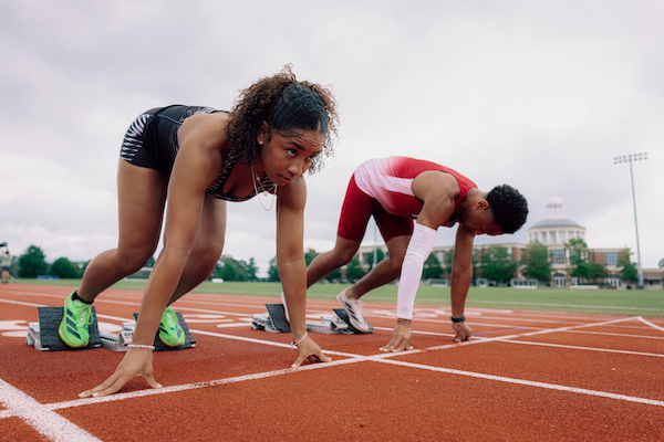 TROY track athletes in the On Your Marks, Set stance with the Trojan Arena in the background. 