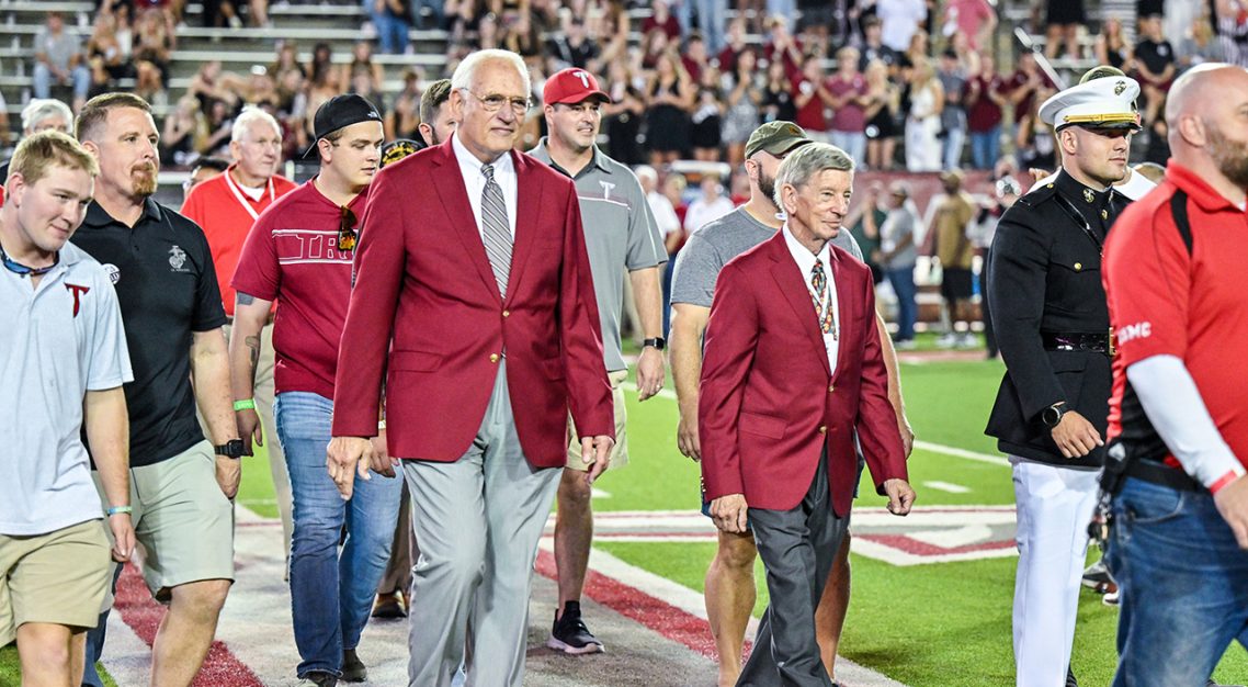 Dr. Jack Hawkins, Jr. walking on thee field at Veteran's Memorial stadium with members of the military. 