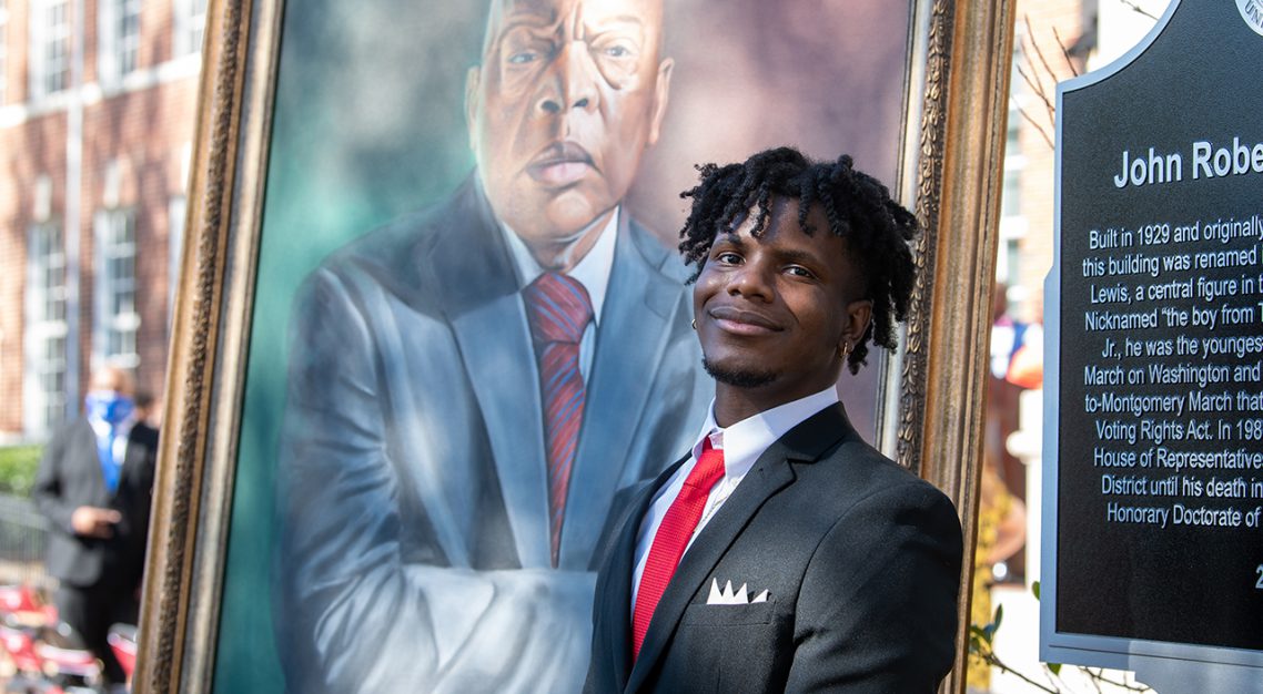 Karvarus Moore standing with his portrait of John Lewis in front of John Lewis hall 