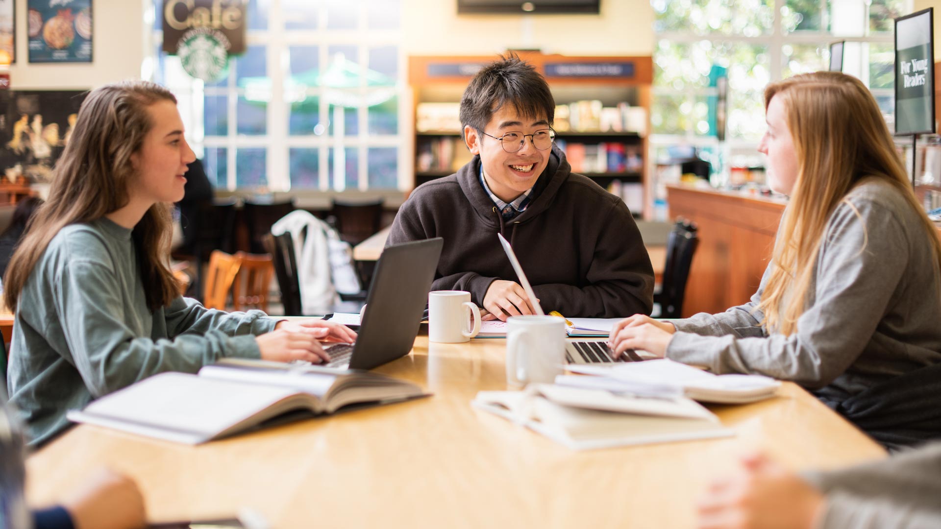 Students in the library, sitting at a table together on computers