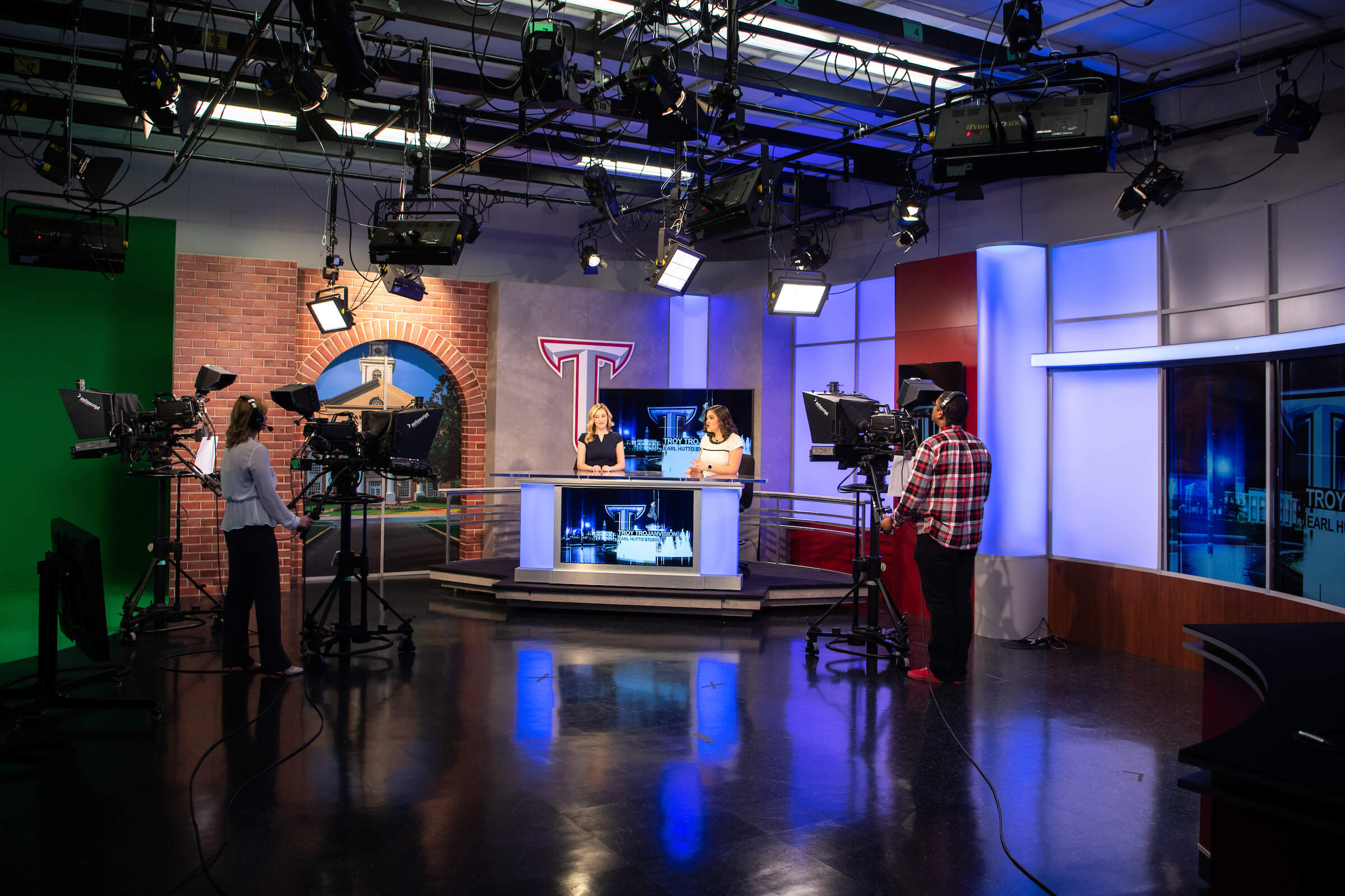  Photo of to journalism students operating television production cameras on a student-run television news set of Troy TrojanVision Nightly News