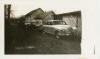 Photograph of three cars near house and garage-like outbuilding